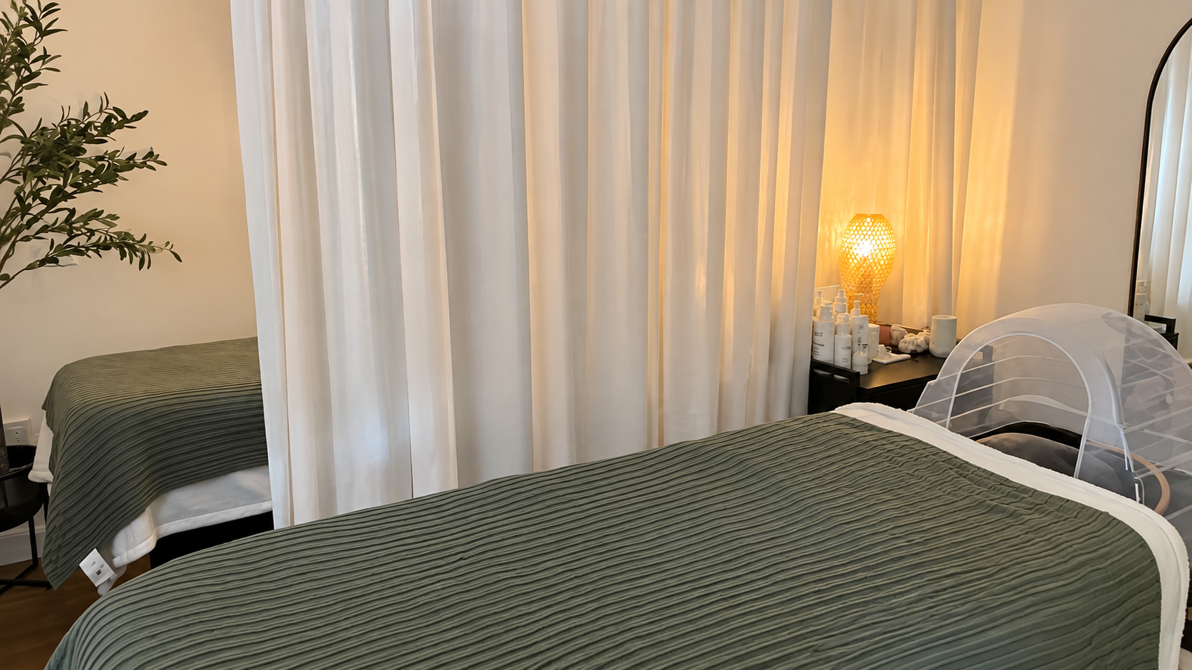 Treatment room with a soft green bed, curtain and facial equipment